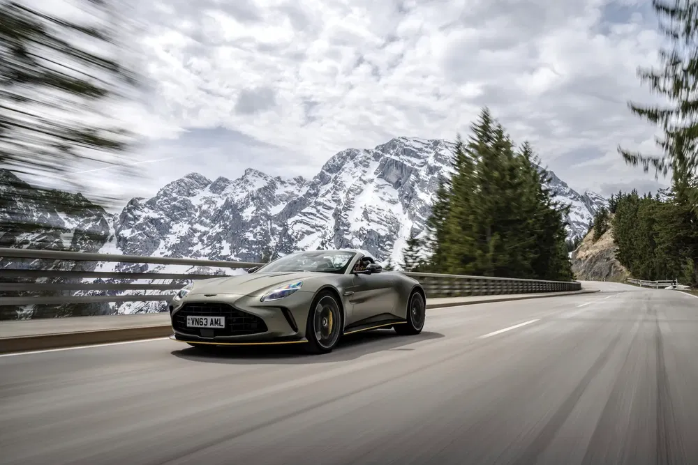 Aston Martin sur route montagneuse, avec arrière-plan alpin majestueux et ciel nuageux.