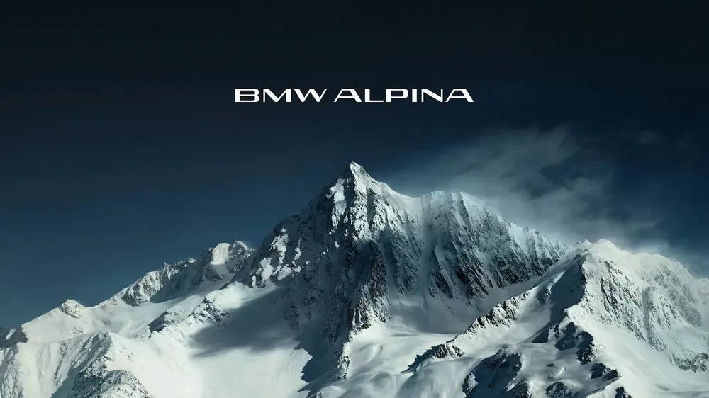 Logo BMW Alpina au sommet enneigé d'une montagne sous un ciel sombre.