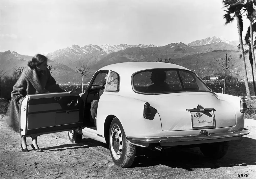 Alfa Romeo Giulietta vintage près des montagnes, femme élégante ouvre une porte.