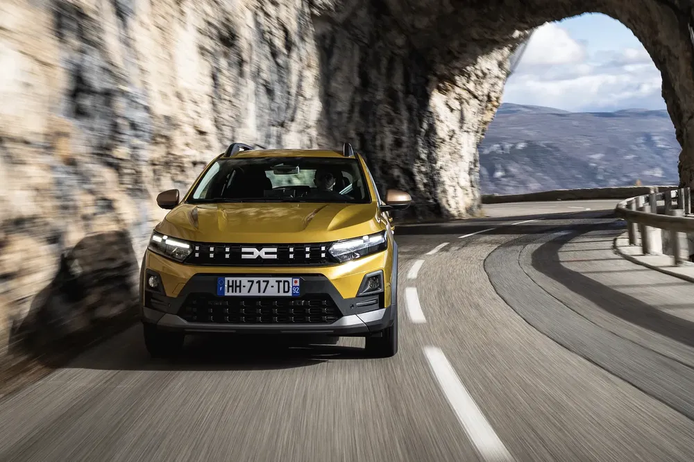 Dacia Sandero jaune roulant sur une route pittoresque avec un tunnel rocheux.