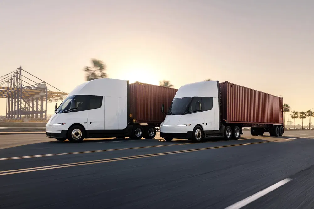 Deux camions Tesla Semi transportant des conteneurs sur une autoroute au coucher du soleil.