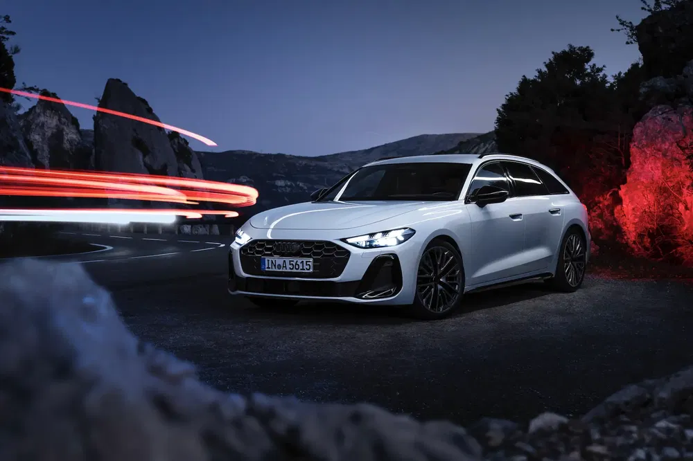 Audi sur route sinueuse avec traînées lumineuses rouges, ambiance nocturne montagneuse.