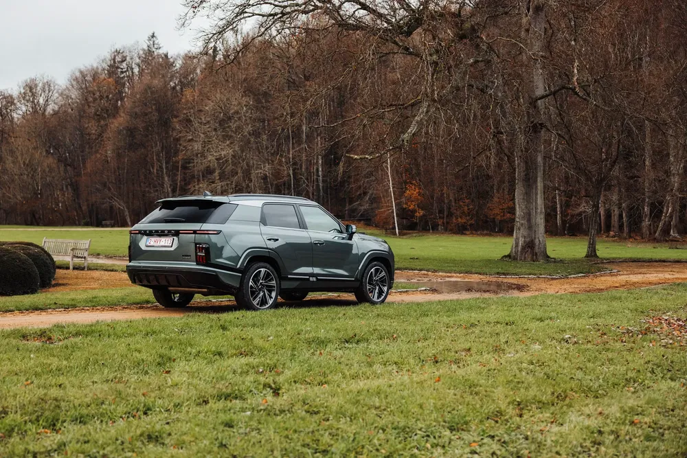 Moderne SUV geparkeerd op zandweg, omringd door bos en bomen op de achtergrond.