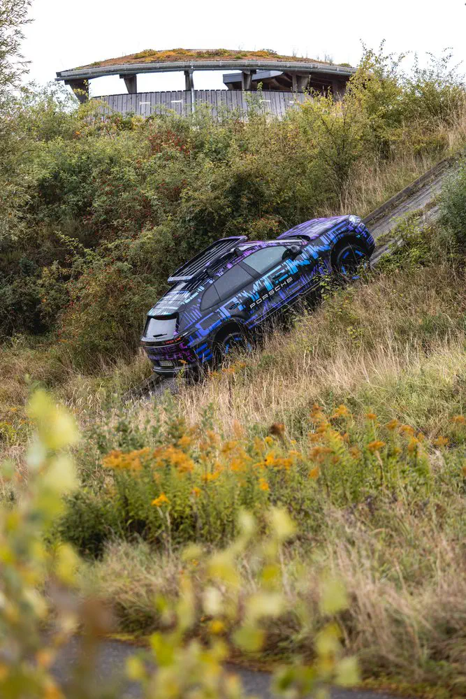 Prototype Porsche SUV beklimt een grashelling, omgeven door weelderige vegetatie.