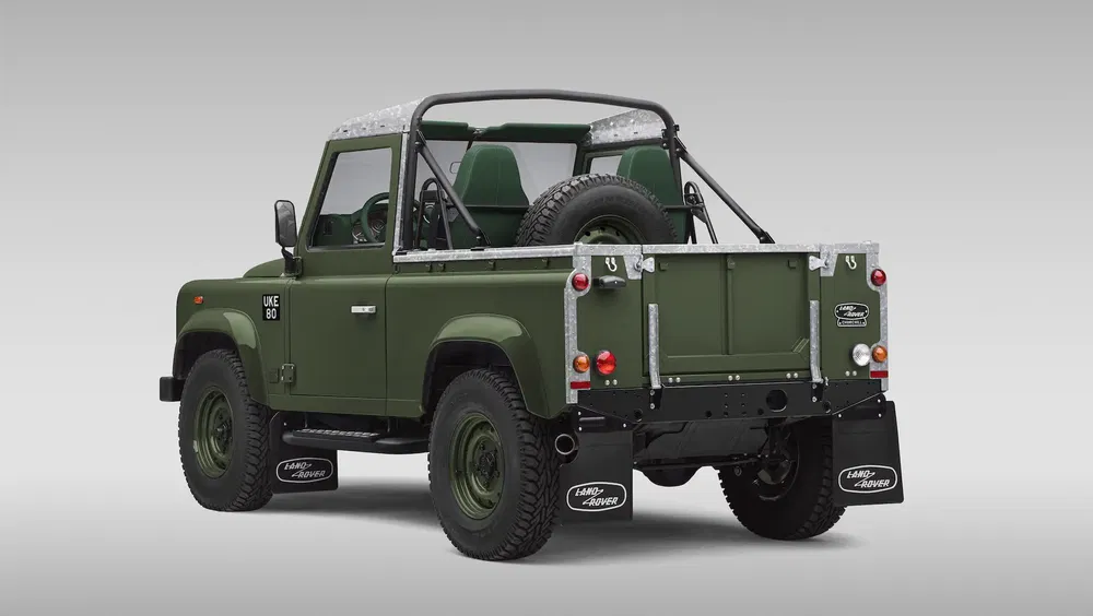 Land Rover Defender vert, toit ouvert, roue arrière visible, fond gris.