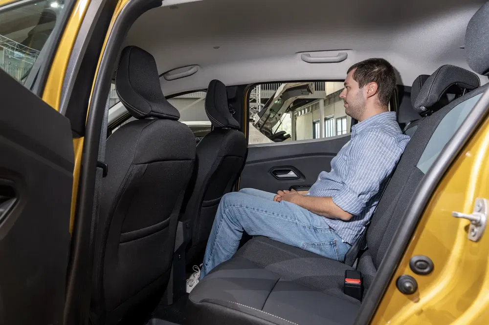 Homme assis à l'arrière d'une Dacia Sandero, intérieur spacieux et confortable.