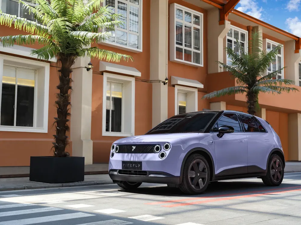 Voiture électrique Firefly violet clair garée devant bâtiment moderne avec palmiers.