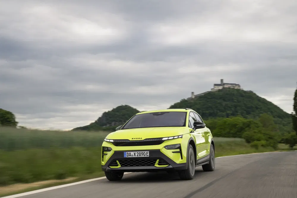 Limoengroene Skoda Enyaq Coupé iV rijdt op landelijke weg, kasteel op de achtergrond.