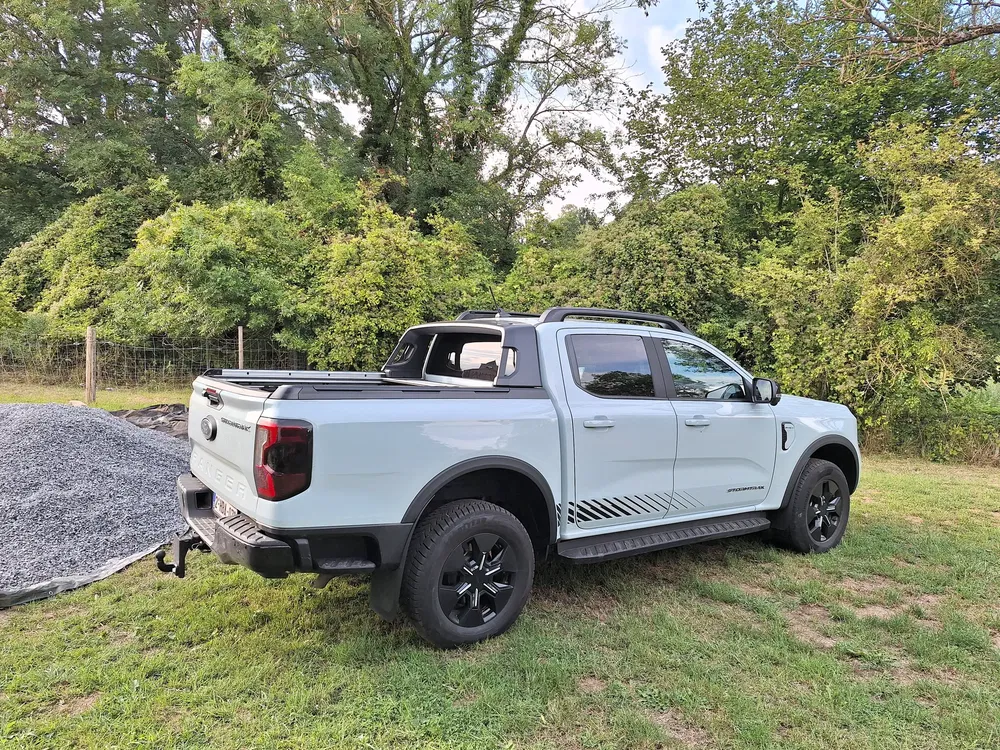 Camionnette Ford Ranger blanche garée sur l'herbe près d'arbres et de pierres.