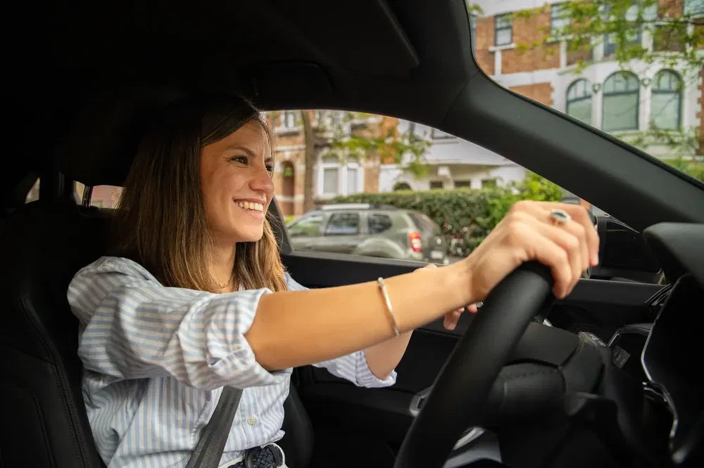 Conductrice souriante au volant d'une voiture moderne en milieu urbain.