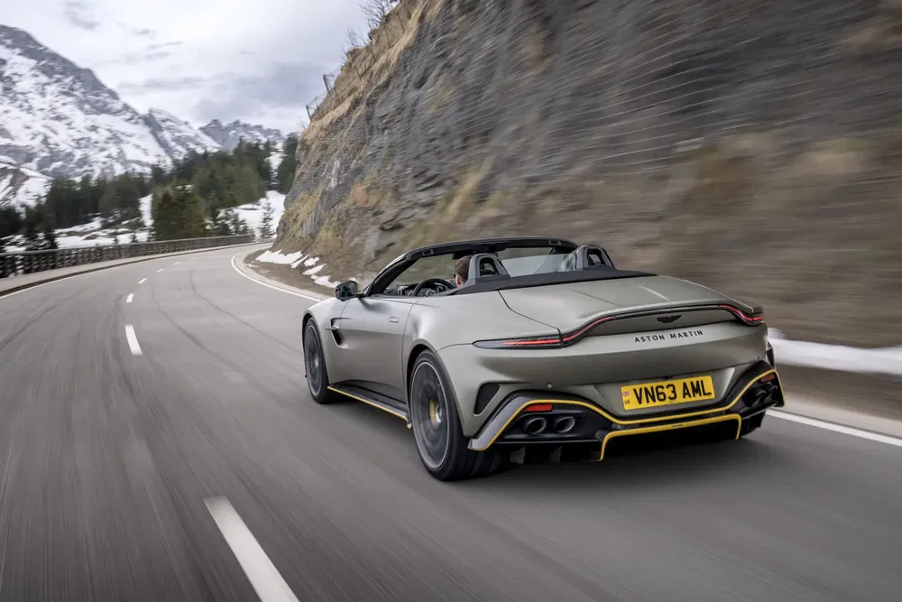 Aston Martin Vantage décapotable sur route de montagne sinueuse enneigée, performance sportive.