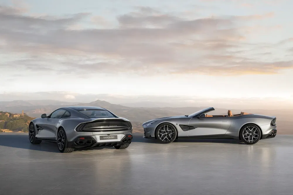 Deux Aston Martin Vanquish modernes, coupé et décapotable, en plein air au coucher du soleil.