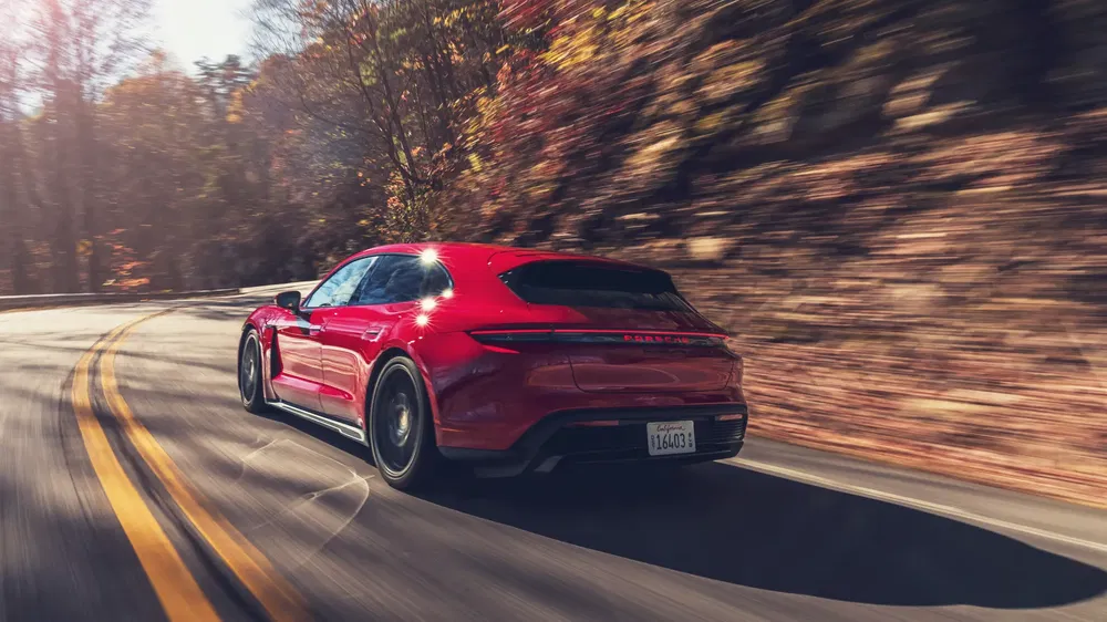 Porsche Taycan rouge roulant sur une route sinueuse entourée de feuilles automnales.