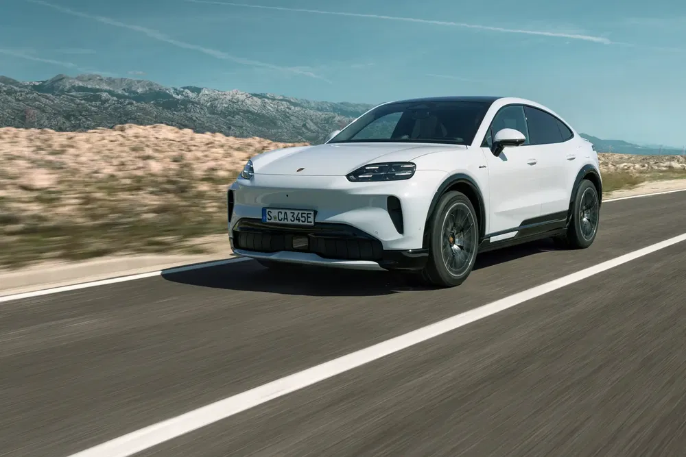 Witte elektrische Porsche Macan rijdt op een schilderachtige weg.