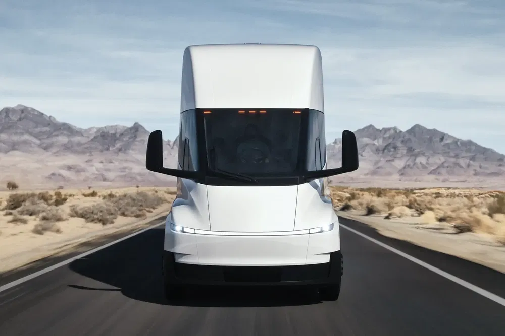 Camion Tesla Semi blanc roulant sur une route désertique avec des montagnes en arrière-plan.