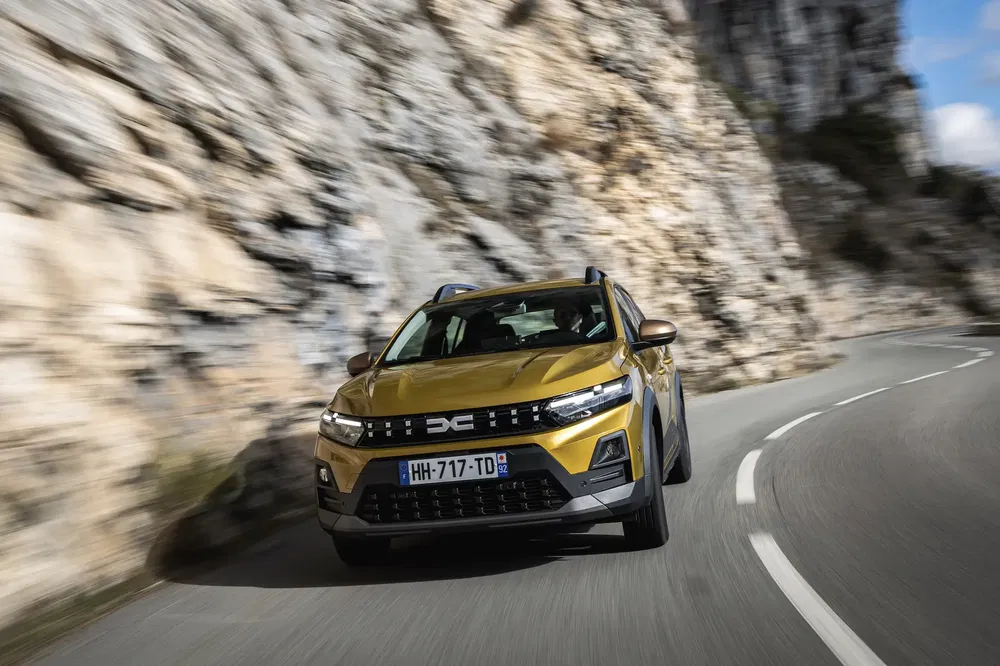 Dacia Duster traversant une route sinueuse entourée de falaises rocheuses.