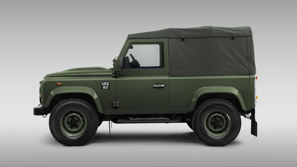 Land Rover Defender vert, vue latérale, toilé, stationné, fond gris.