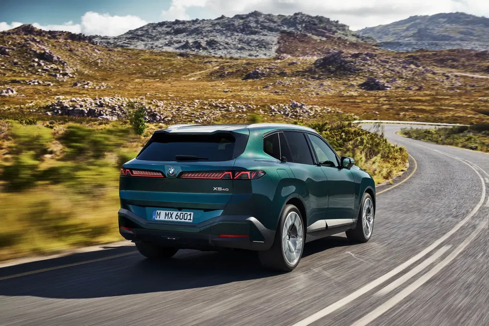 BMW X5 eDrive verte sur route sinueuse de montagne, arrière avec feux distinctifs.