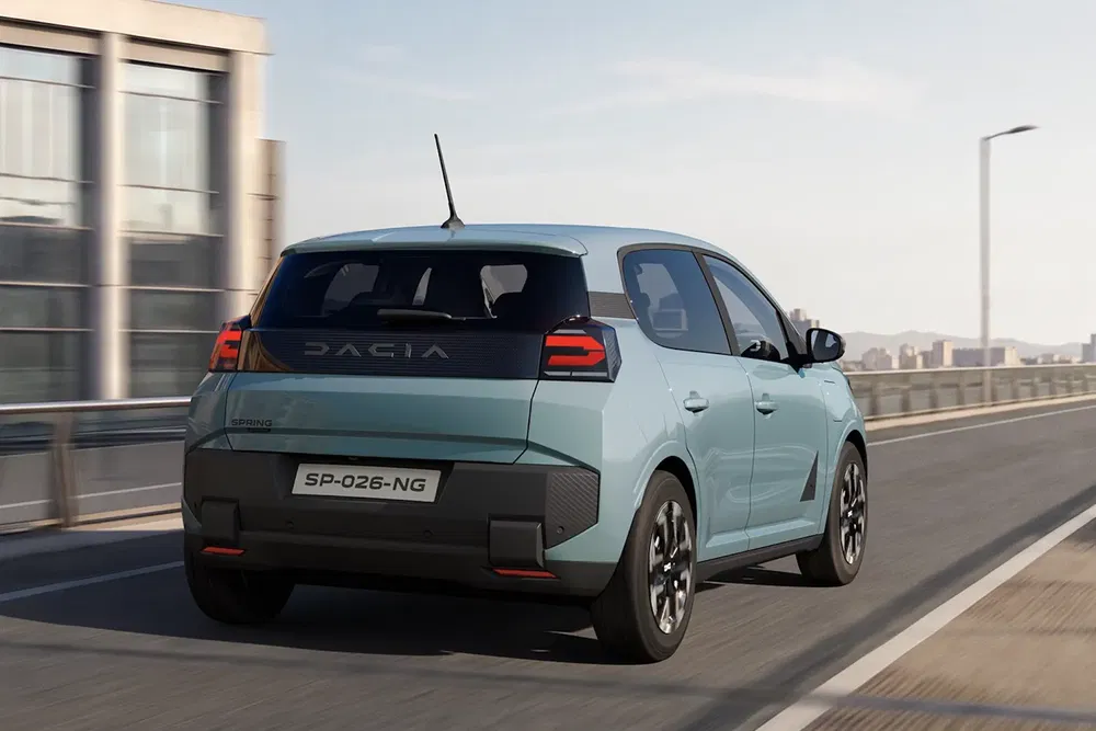 Dacia Spring électrique roulant sur une route urbaine, vue arrière dynamique.