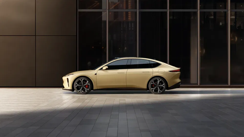 Berline électrique NIO ET7 beige garée devant un immeuble moderne vitré.