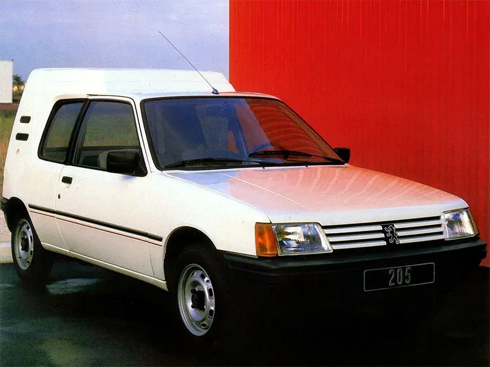 Peugeot 205 fourgonnette blanche devant un mur rouge, modèle emblématique des années 1980.