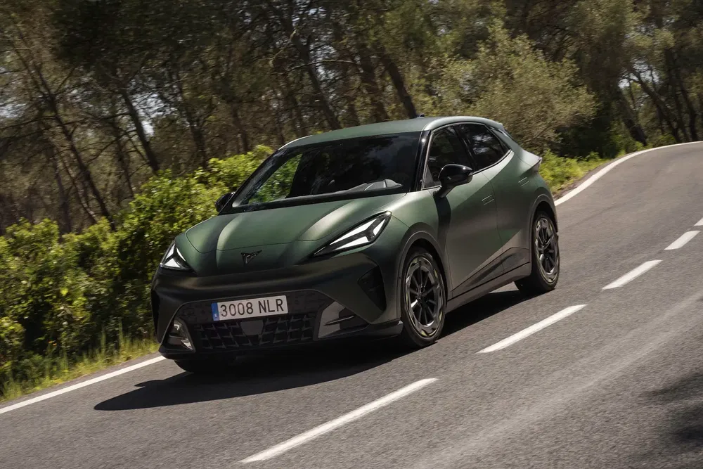 Groene Cupra Born rijdt op kronkelige weg omgeven door bomen, modern sportief ontwerp.