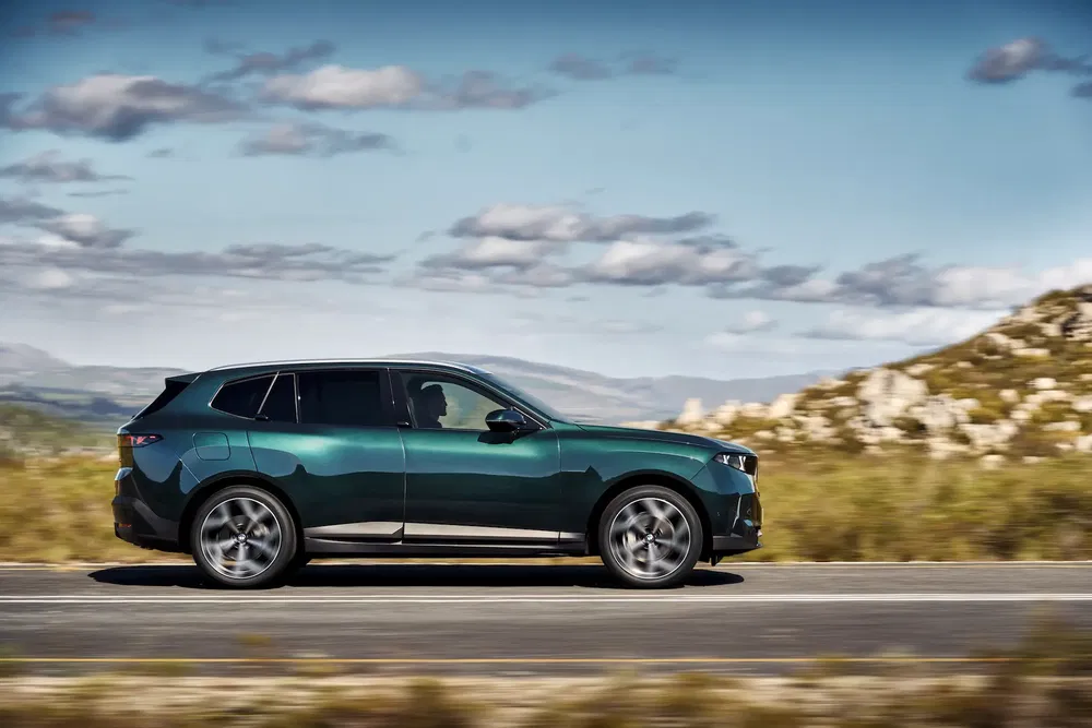 BMW iX vert roulant sur une route panoramique par une journée ensoleillée.