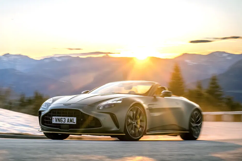 Aston Martin DBS Volante roulant au coucher du soleil sur une route de montagne enneigée.