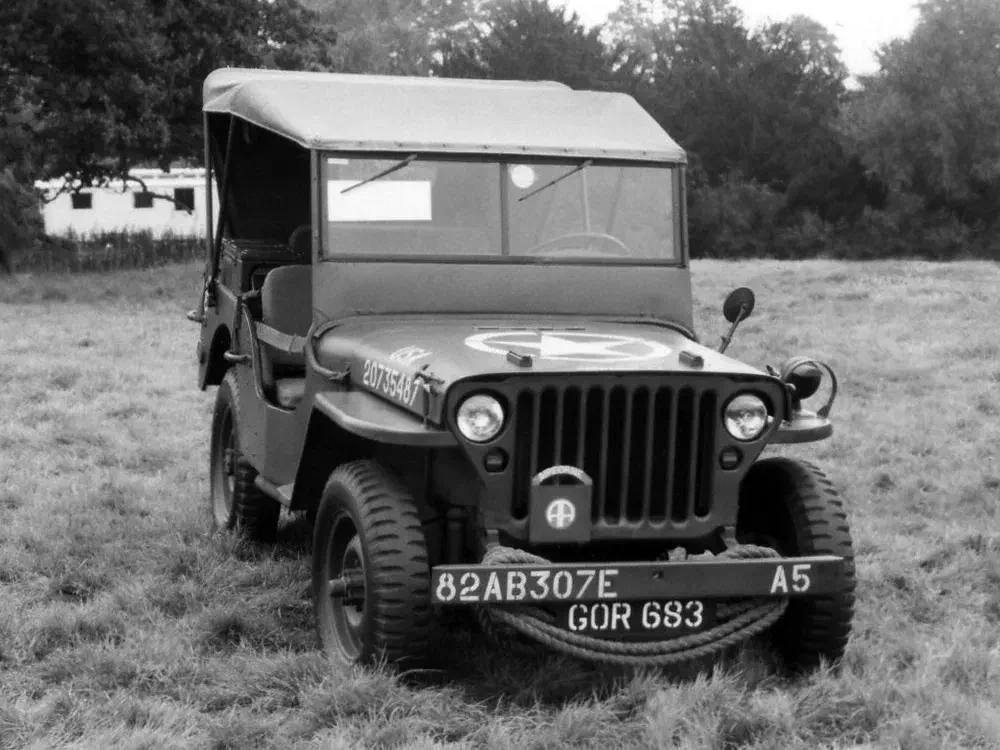 Vintage Jeep Willys op grasveld, militair embleem op de motorkap, nabij bos.