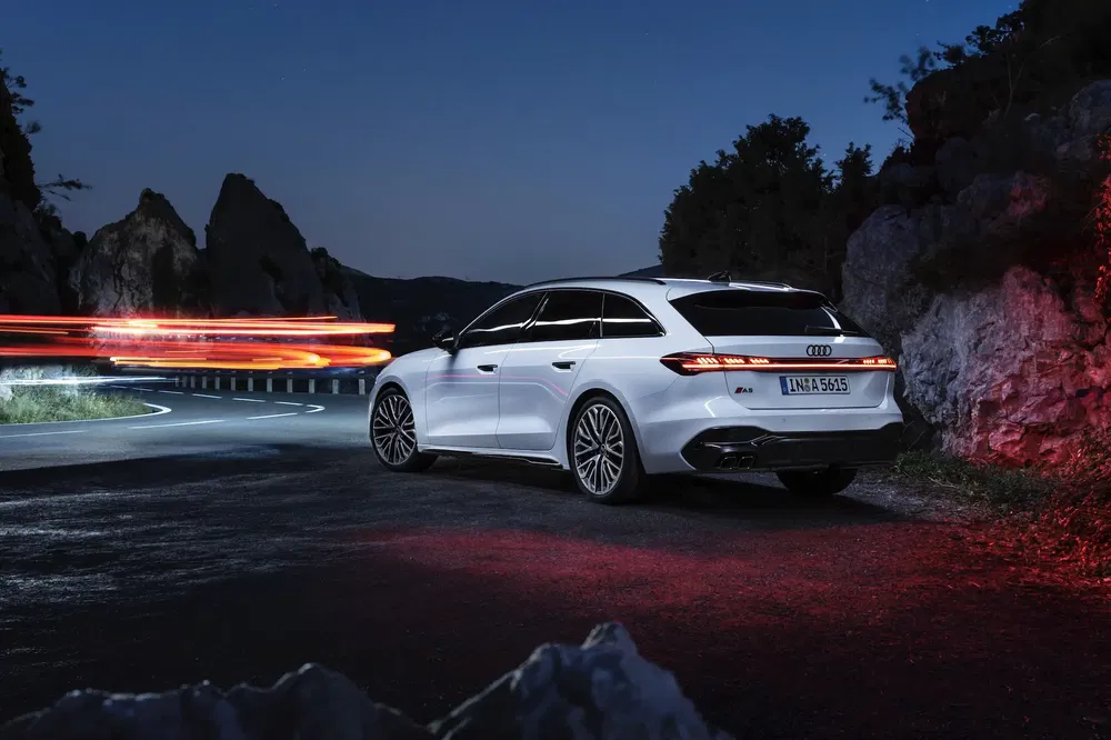 Audi A6 Avant 2024 sur route sinueuse nocturne avec feux arrière allumés.