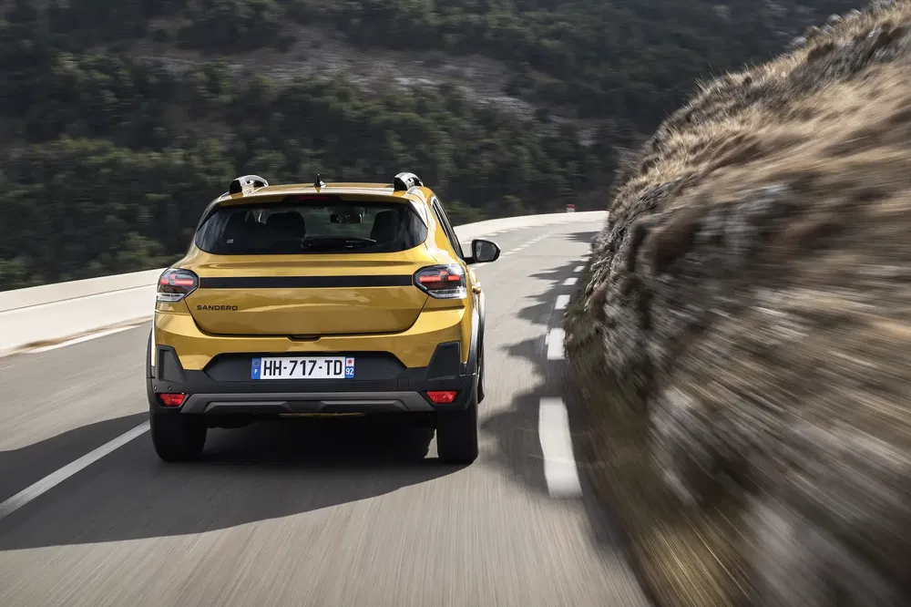 Dacia Sandero jaune sur route sinueuse de montagne, vue arrière dynamique.