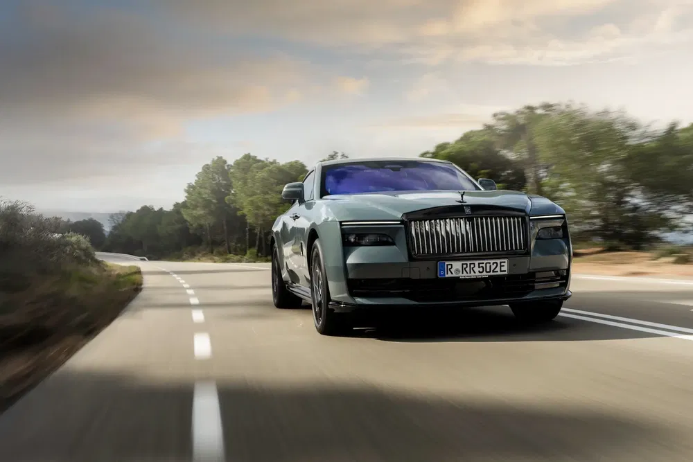 {"fr":"Rolls-Royce électrique sur route sinueuse bordée d'arbres sous ciel dramatique.","nl":"Elektrische Rolls-Royce op bochtige weg omringd door bomen onder dramatische lucht."}