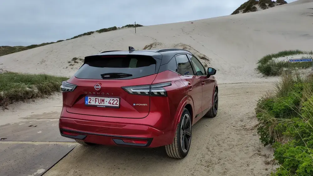 Rode Nissan Qashqai e-Power geparkeerd op zandpad in de duinen.