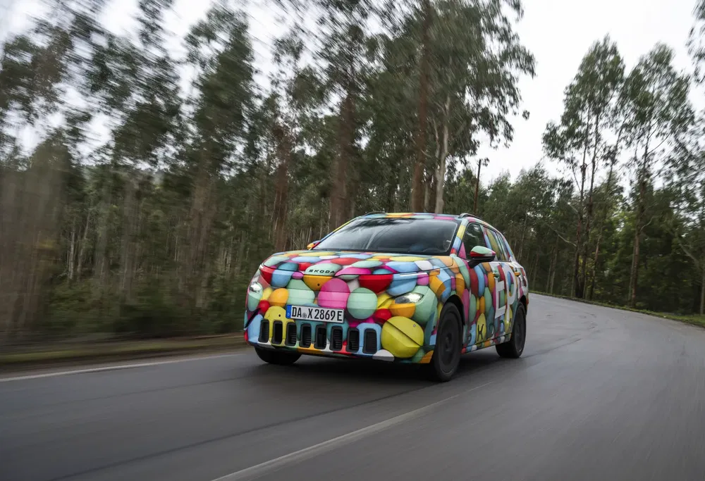 Skoda SUV met kleurrijke camouflage rijdt op weg omringd door bomen, testend rijprestaties.