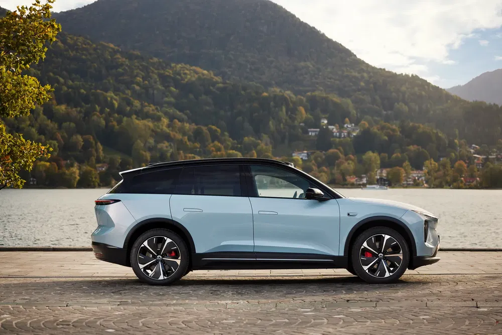 SUV Aiways U6 électrique au bord d'un lac avec montagnes en arrière-plan.