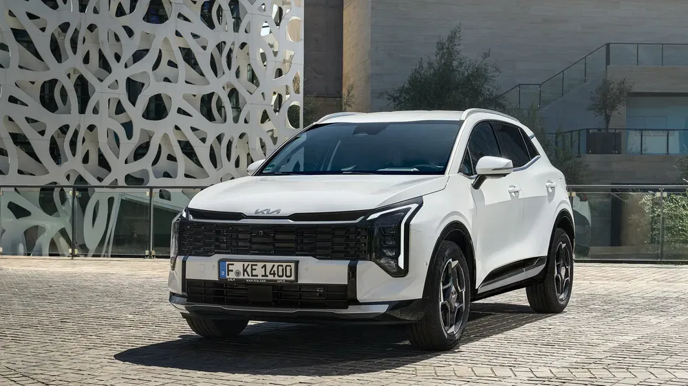 SUV Kia Sportage blanc stationné devant un bâtiment moderne au design futuriste.