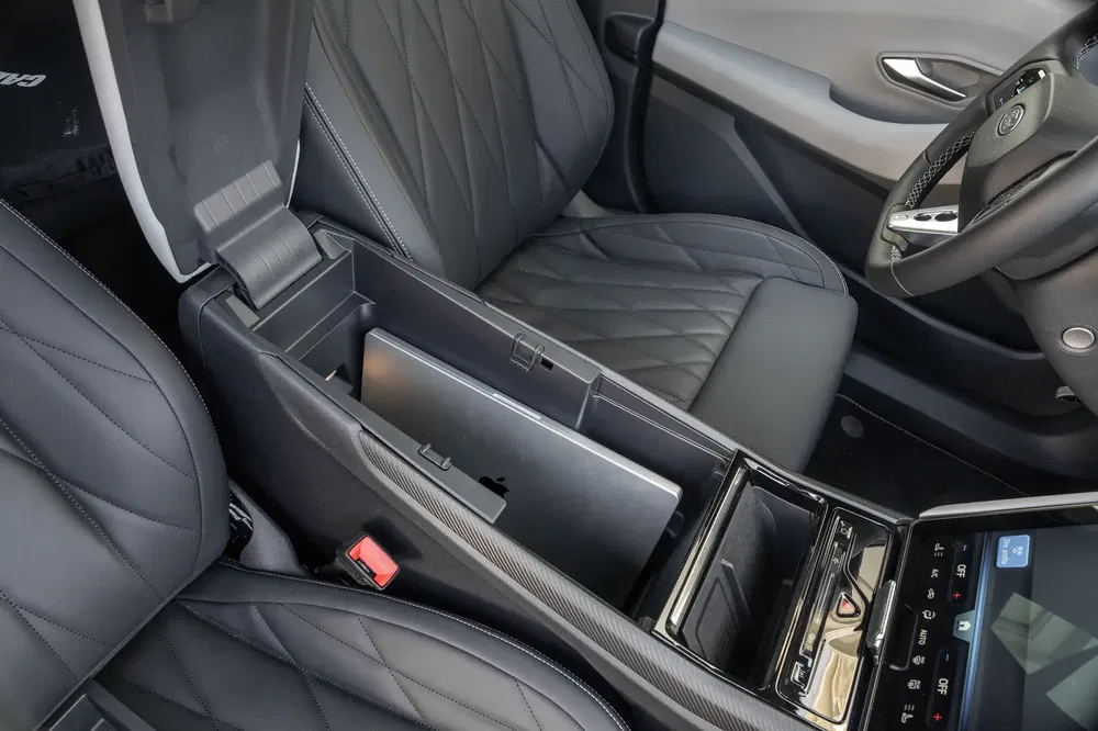 Intérieur de voiture avec console centrale contenant un ordinateur portable Apple, sièges en cuir noir.