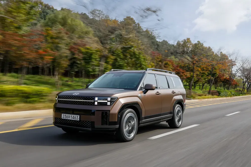 Robuuste bruine Hyundai SUV op weg omringd door herfstbomen, modern design.