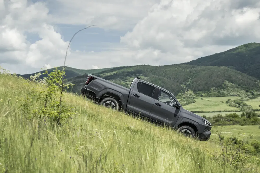 Pickup Toyota hilux grise descendant une colline herbeuse avec des montagnes à l'arrière-plan.