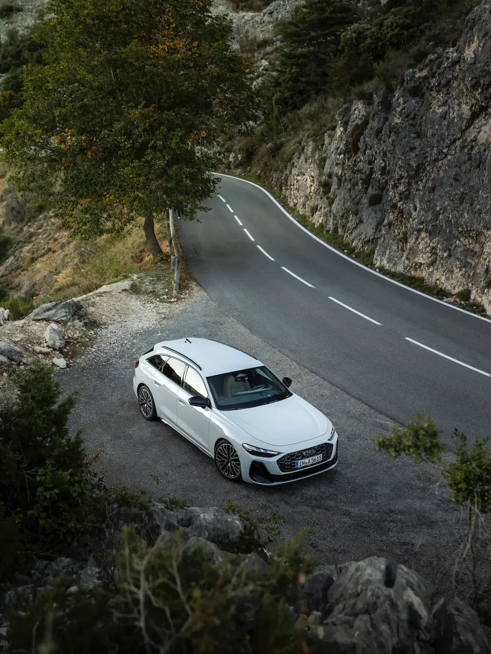 Audi station wagon blanche garée près d'une route de montagne sinueuse et forestière.