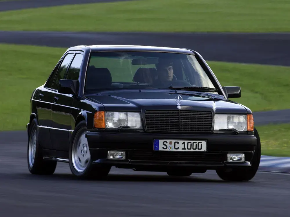 Mercedes-Benz 190E noire conduisant sur piste de course rapide.