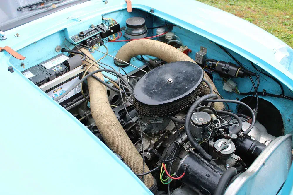 Moteur de voiture classique avec filtre à air rond et câblage vintage dans un compartiment bleu.