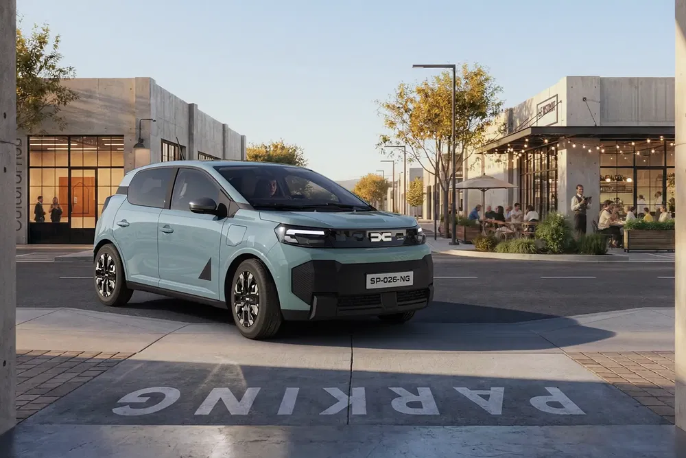 Voiture Dacia Spring 2023, grise, garée dans une rue urbaine moderne et ensoleillée.