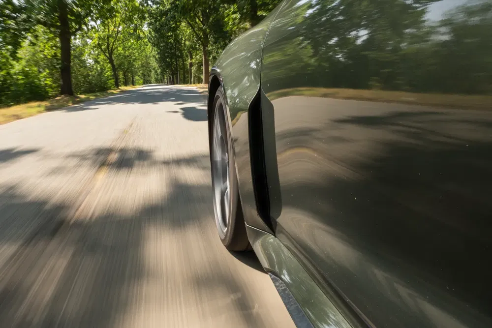 Zijaanzicht van een auto die snel rijdt op een met bomen omzoomde weg.