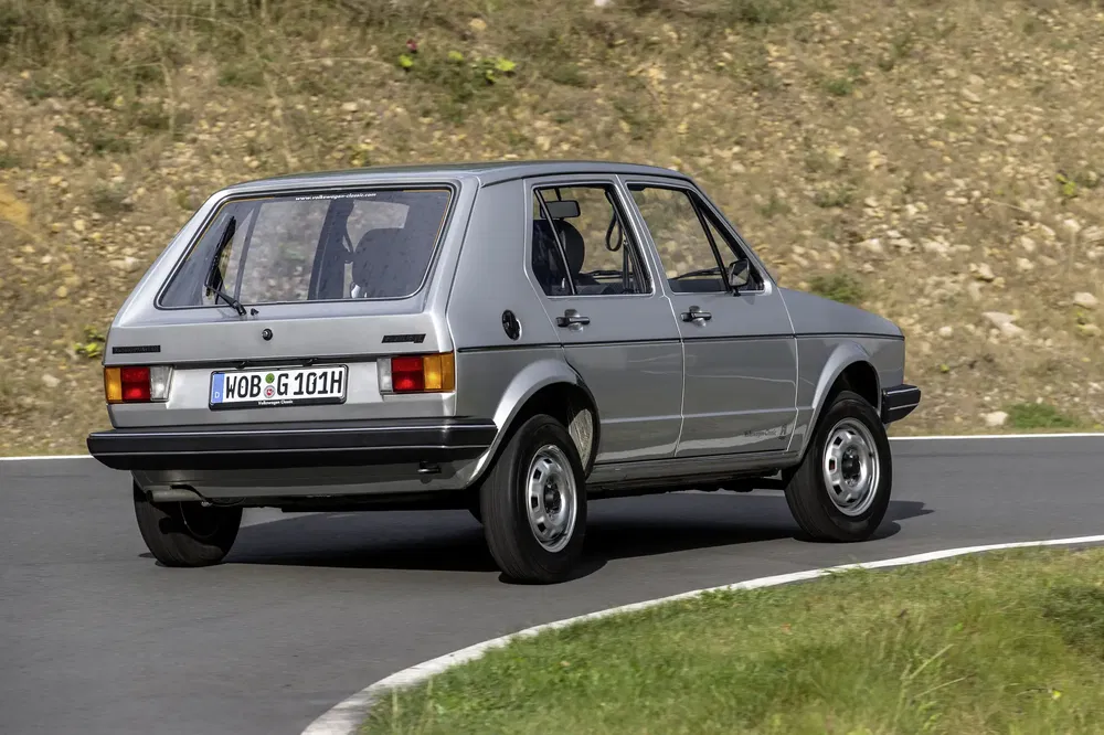 Zilverkleurige Volkswagen Golf uit de jaren '80 op een kronkelige weg, achteraanzicht.