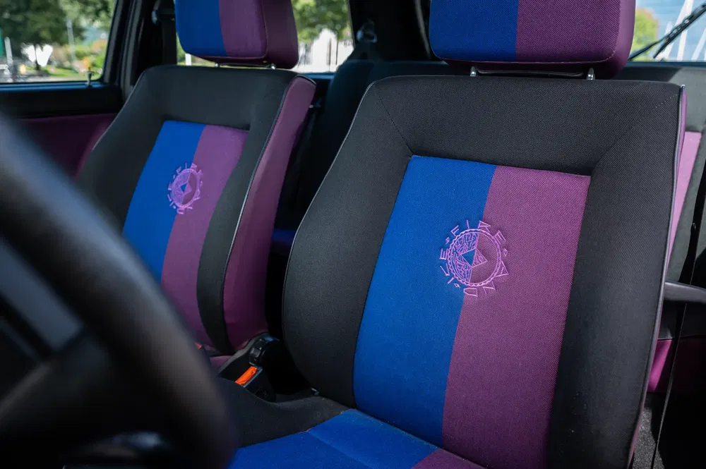 Auto-interieur met paarse en blauwe stoelen, opvallend geborduurd logo in het midden.