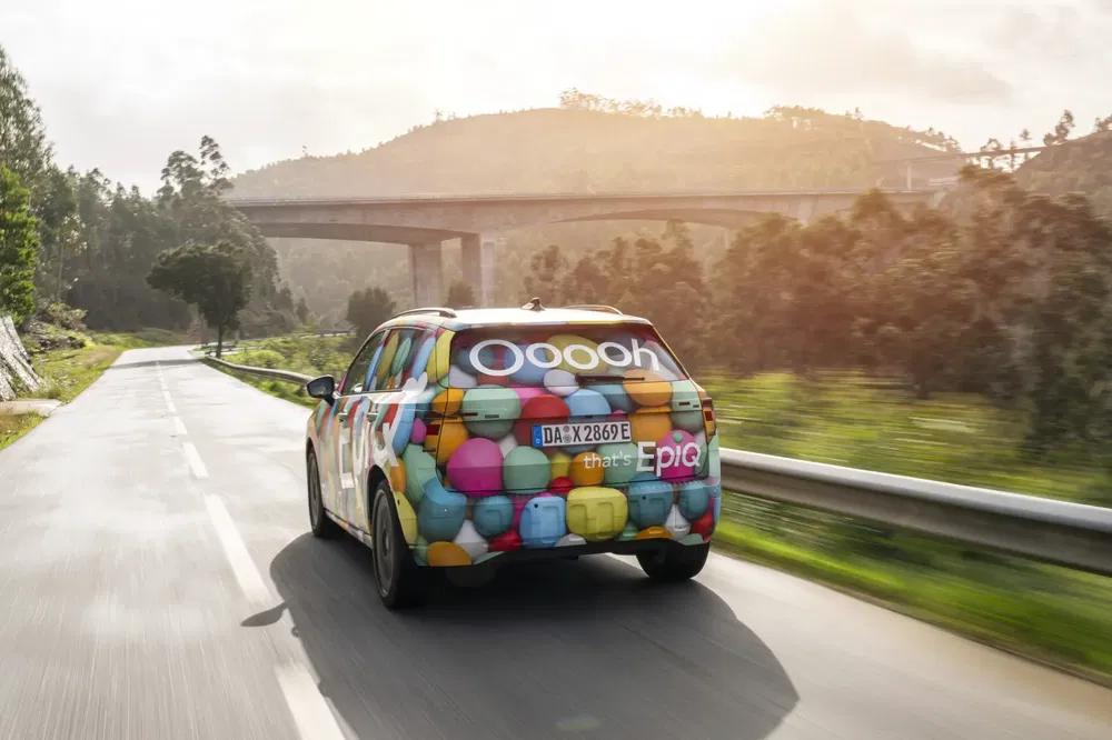 Kleurrijke auto op weg, brug op achtergrond, zonnig groen landschap.