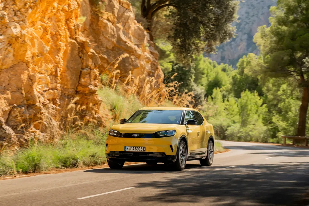 Gele Ford Explorer rijdend op een bochtige weg omringd door rotsen en groen.
