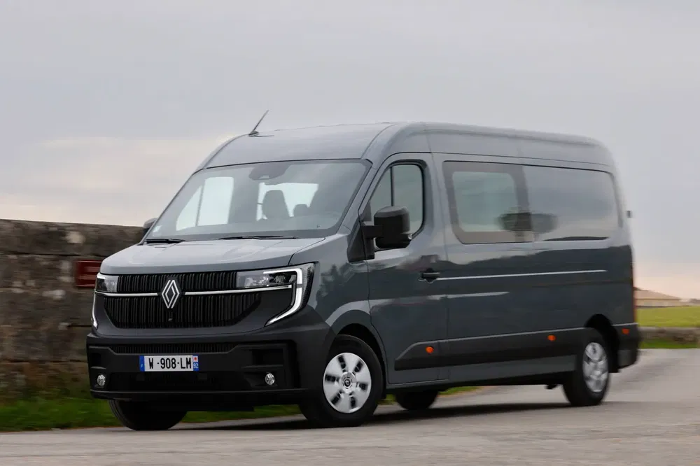 Grijze Renault Master rijdend op een landweg met bewolkte lucht.