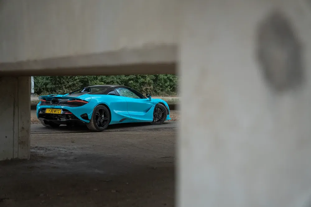 McLaren 720S bleue garée sous un pont en béton, arrière dynamique et élégant.
